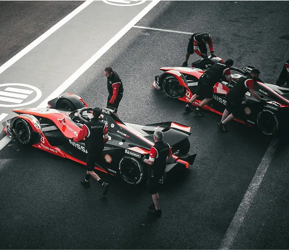 A group of men stands beside black and red racing cars, showcasing their vehicles in a competitive atmosphere.