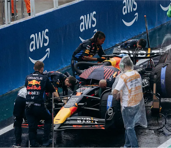 A red Bull Racing car is being serviced by mechanics in a busy garage environment.