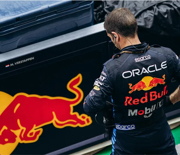 A man in a red bull uniform stands beside a prominent red bull logo, showcasing brand identity and team spirit.