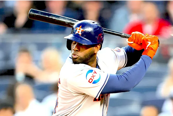 A baseball player stands confidently, gripping a bat, ready to take a swing on the field.