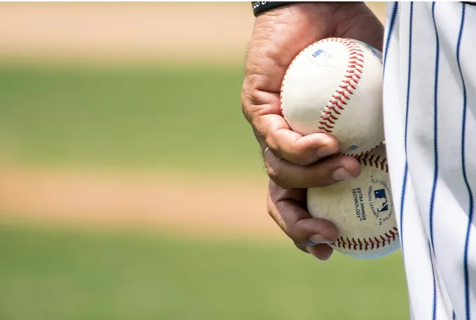 A baseball player stands confidently, gripping two baseballs in his hands, ready for the game ahead.