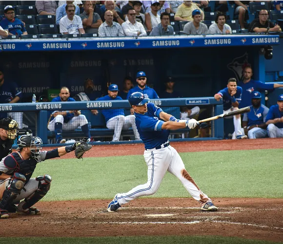 A baseball player in mid-swing, striking a ball with a bat on a sunny field.