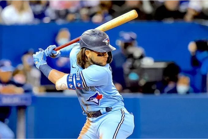 A baseball player in mid-swing, striking a ball with a bat on a sunny field.