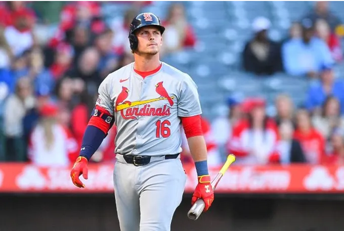 A baseball player in a red uniform stands ready, holding a bat, poised for action on the field.