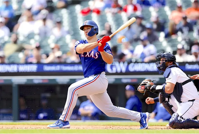 A baseball player in mid-swing, striking a ball with a bat on a sunny field.