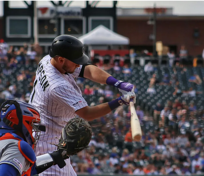 A baseball player in mid-swing, striking a ball with a bat on a sunny field.