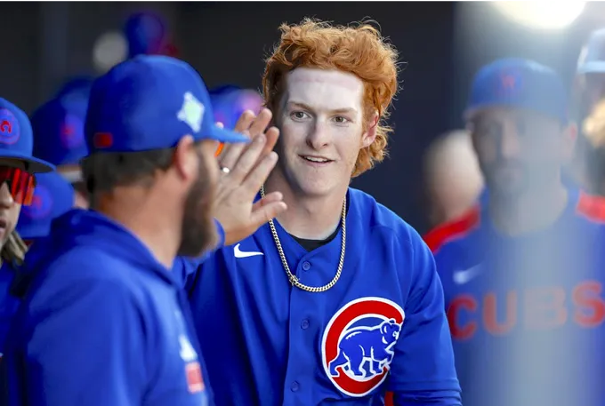 A baseball player with red hair wearing a blue uniform stands ready to bat on the field.