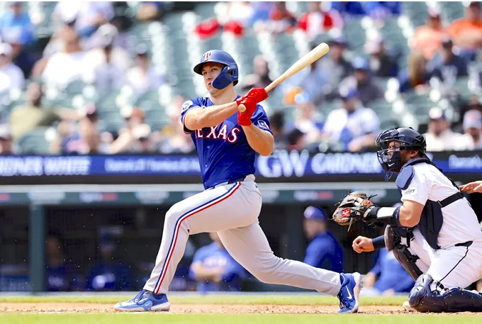 A baseball player in mid-swing, striking a ball with a bat on a sunny field.