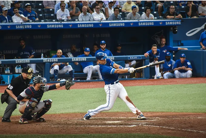 A baseball player in mid-swing, striking a ball with a bat on a sunny field.