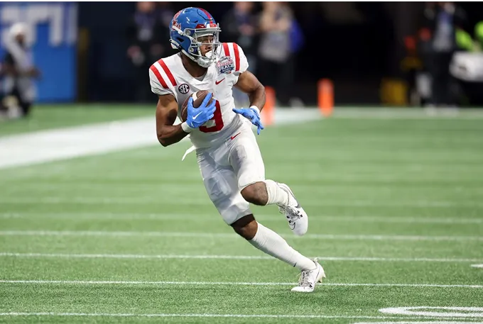 A football player sprinting with the ball across a green field during a game.